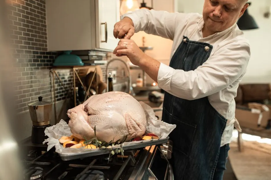 A chef seasons a whole turkey in a modern kitchen, preparing for Thanksgiving.